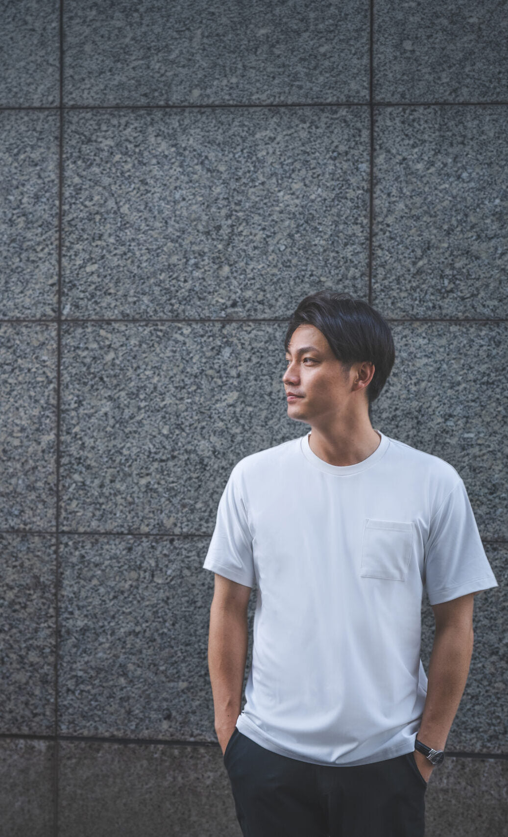 壁の前に立つ、白いTシャツ姿の男性